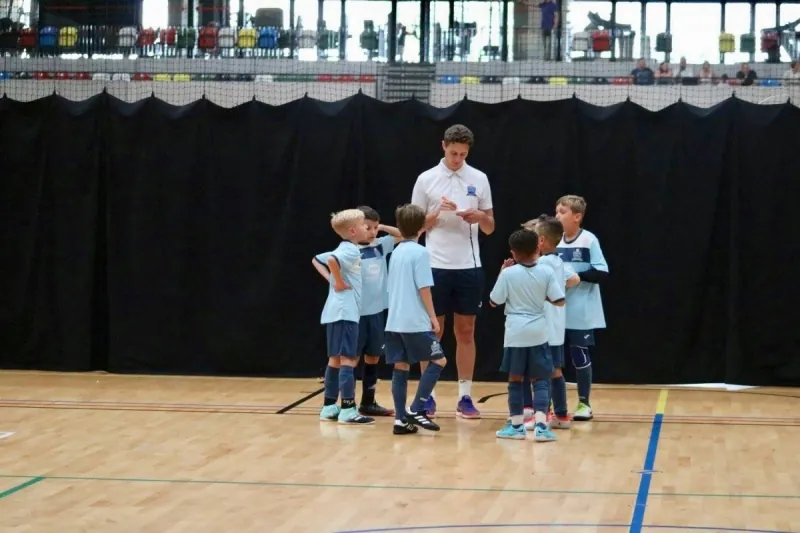 A coach briefing a group of young players on the indoor court
