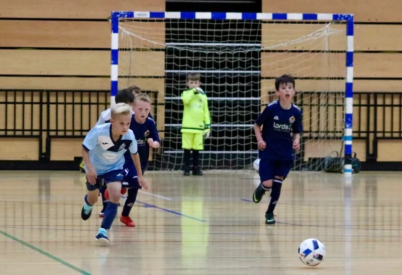 Young futsal players running towards the ball in front of the goal