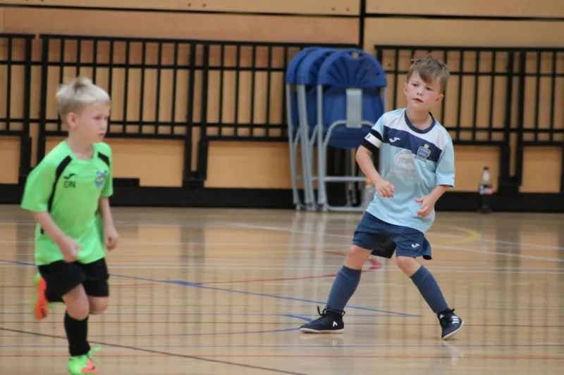 Two young players in light-blue and green kits during a futsal match