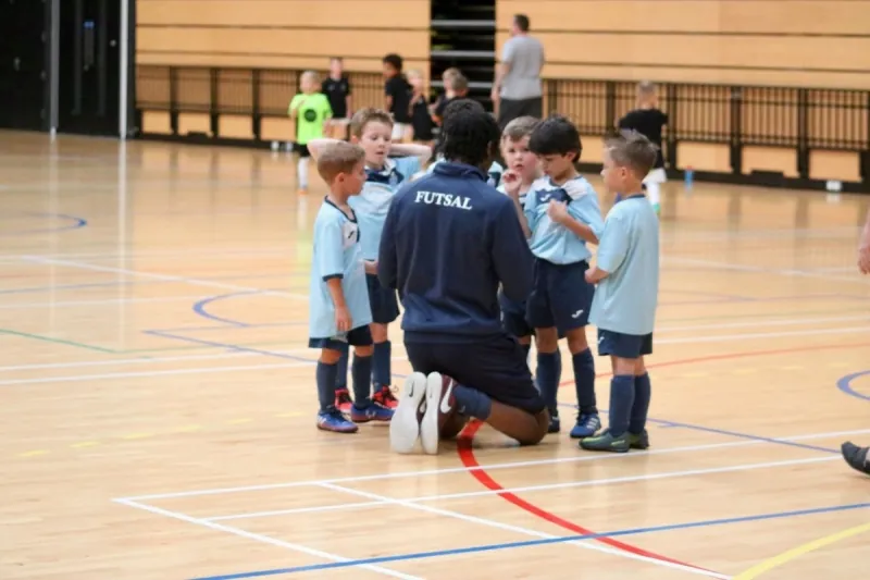 A coach kneeling to speak with a group of young Braintree players