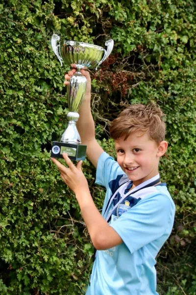 A young player lifting a trophy while wearing a medal