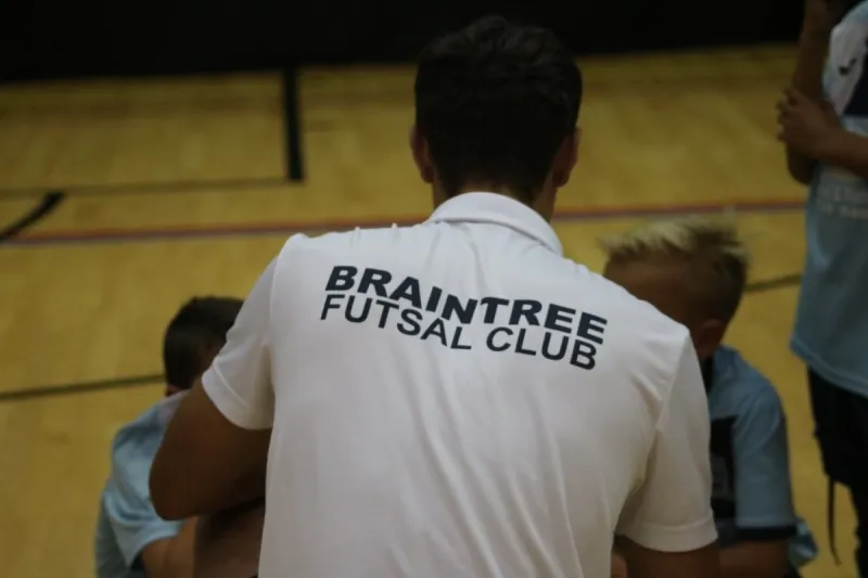 A coach in a Braintree Futsal Club shirt talking with young players